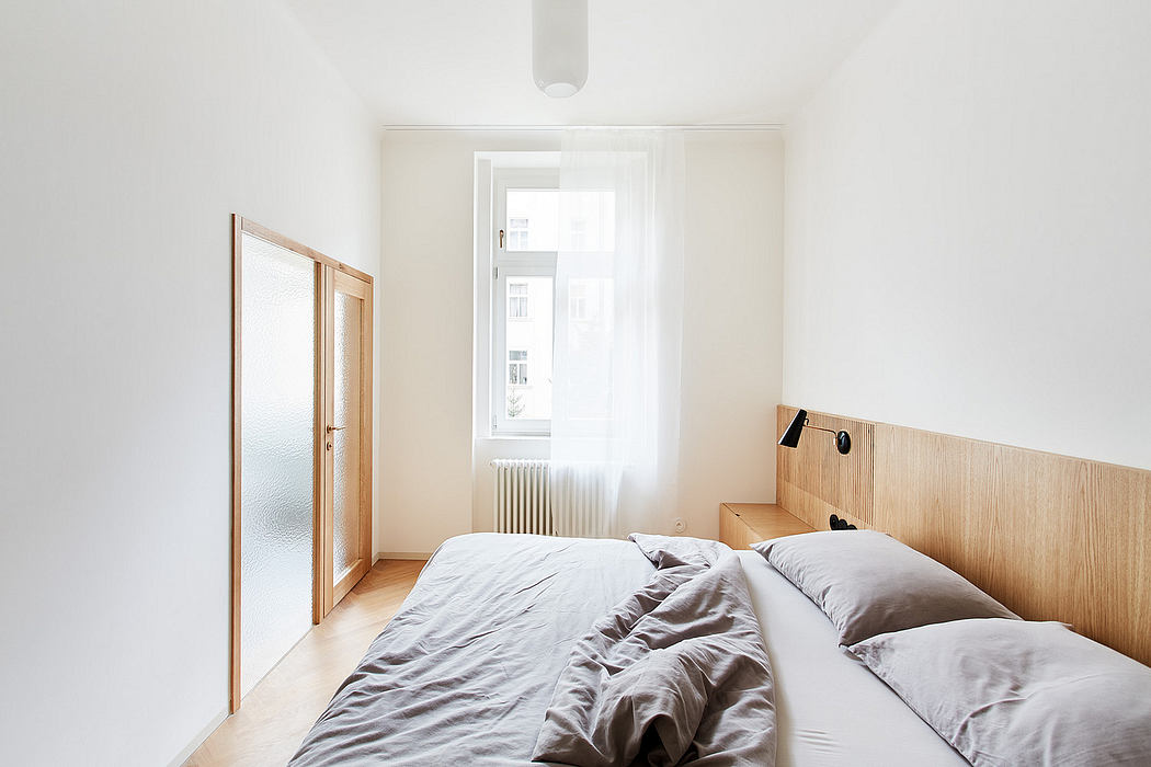 Minimalist bedroom with wooden headboard, large window, and crisp white walls.
