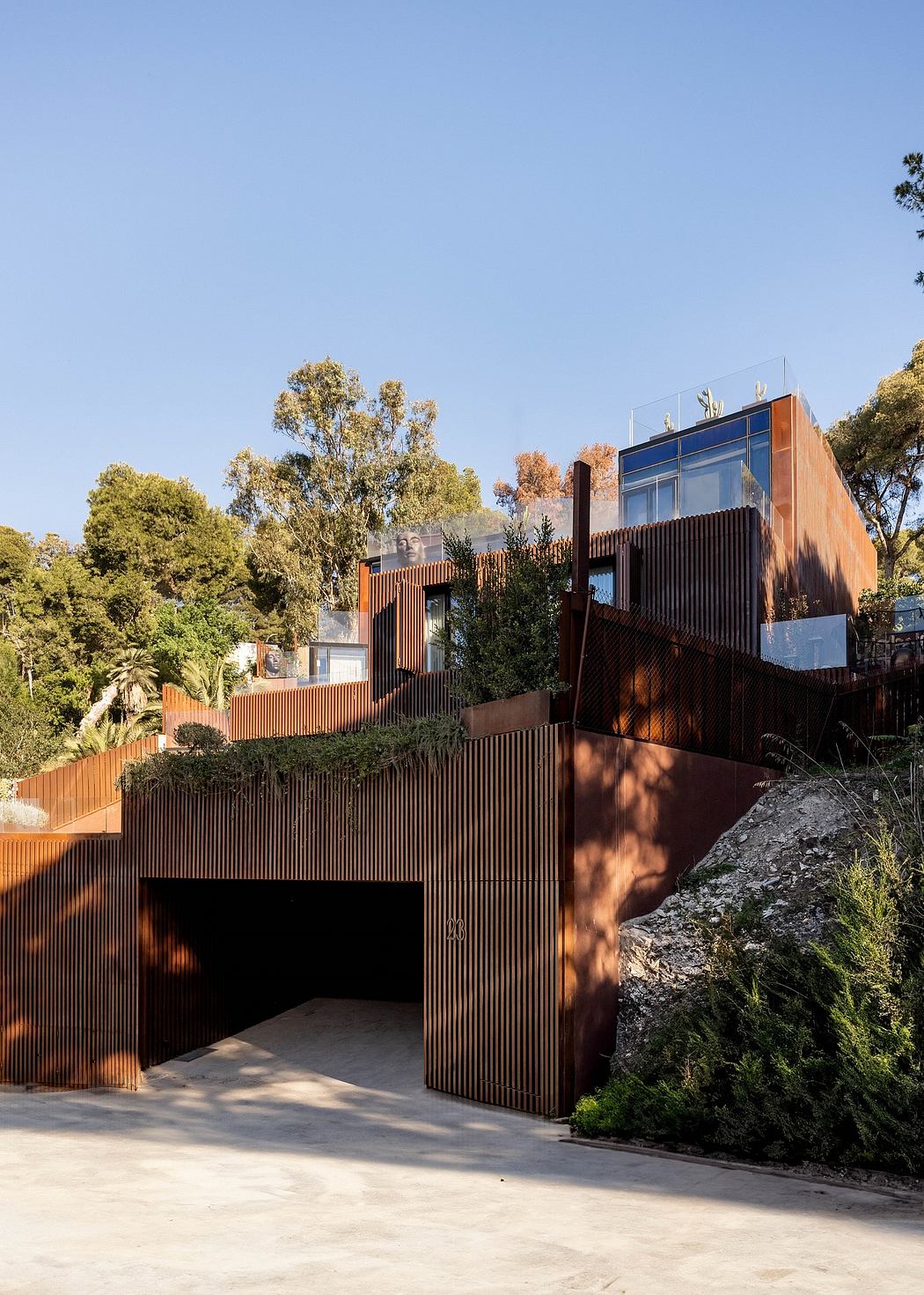 Modern multilevel building with wooden facade and glass panels, surrounded by lush greenery.