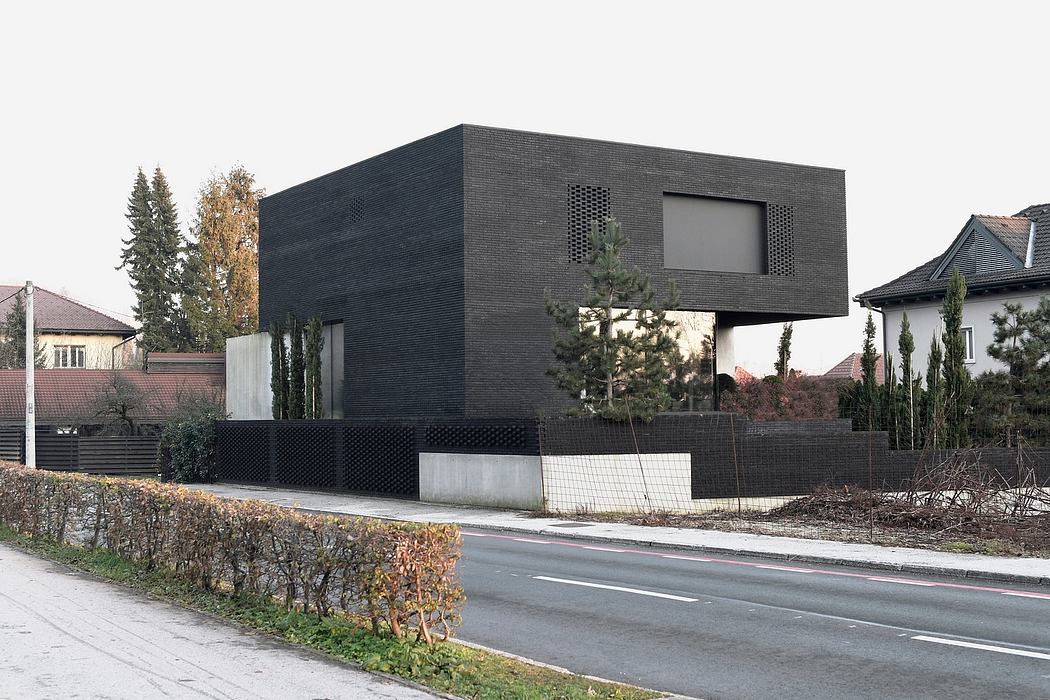 Angular, geometric, black facade with recessed windows and plant features.