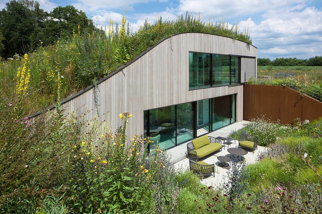 A modern, wood-clad home with a green roof, large windows, and an outdoor seating area.