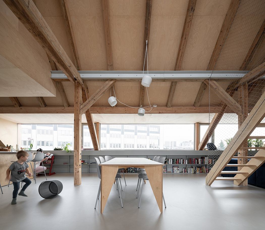 Spacious open-plan interior with exposed wooden beams, bookshelves, and minimalist furnishings.