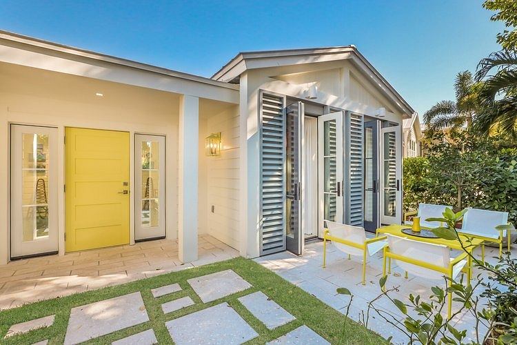 Bright, modern exterior with yellow door and shuttered windows overlooking lush greenery.