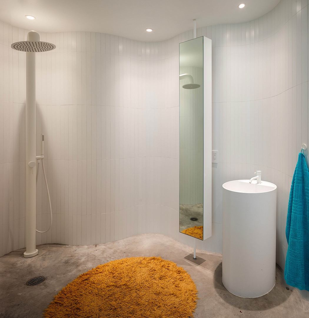 A modern, minimalist bathroom with a large rain shower, pedestal sink, and shag rug.