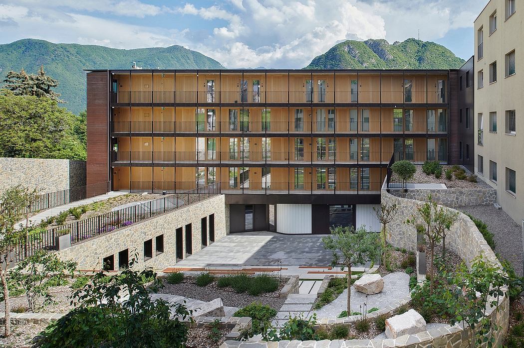 Modern, terraced apartment building with wooden facades, balconies, and landscaped courtyard against mountainous backdrop.