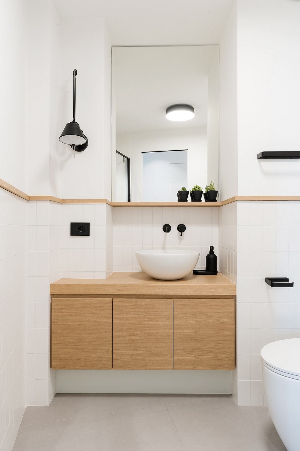 A clean, minimalist bathroom with a wooden vanity, a white basin, and a wall-mounted mirror.