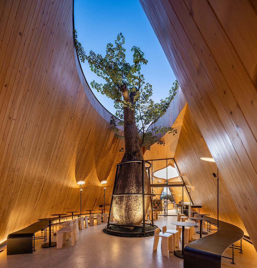 A modern interior with a large tree growing through the center, surrounded by curved wooden walls and seating areas.