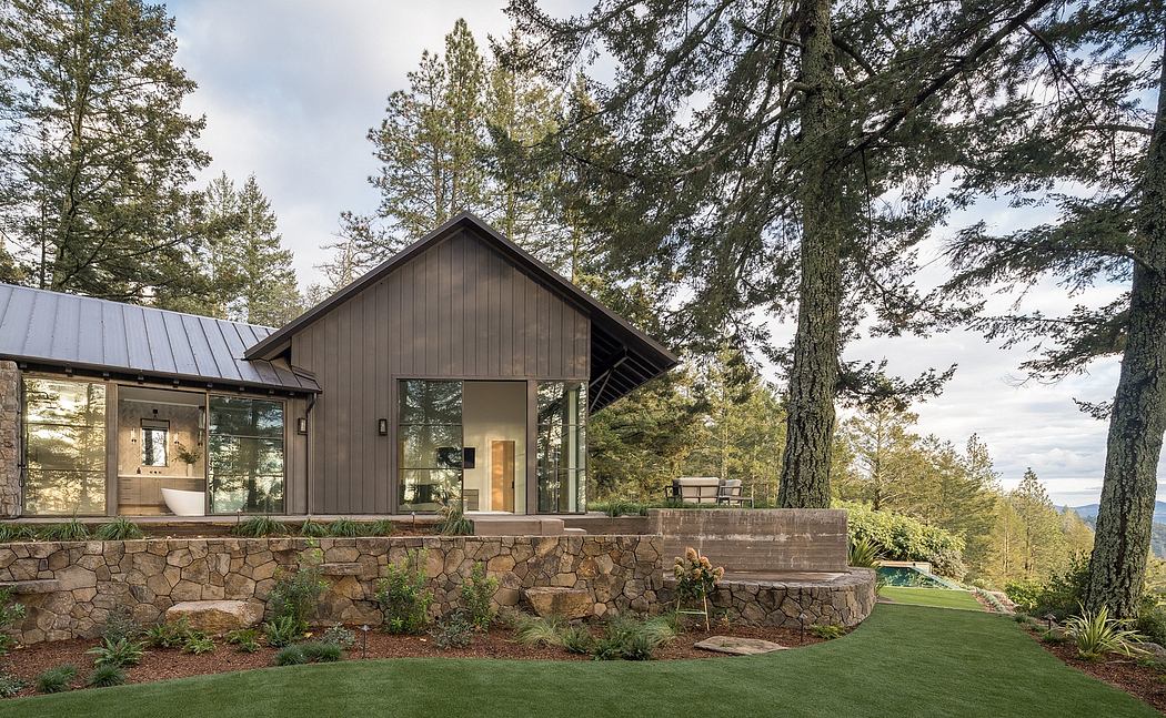 A modern rustic cabin nestled in the woods, featuring a stone foundation, large windows, and a metal roof.