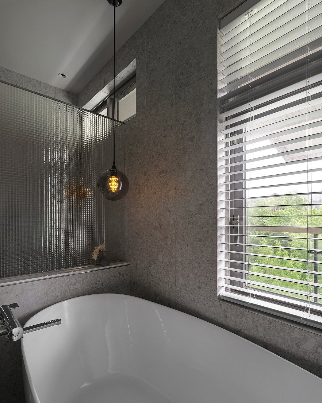 A modern bathroom with gray concrete walls, a freestanding bathtub, and a large window with blinds.