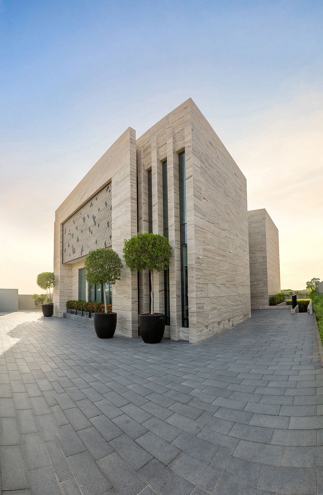 A modern architectural building with a geometric facade, surrounded by potted plants.