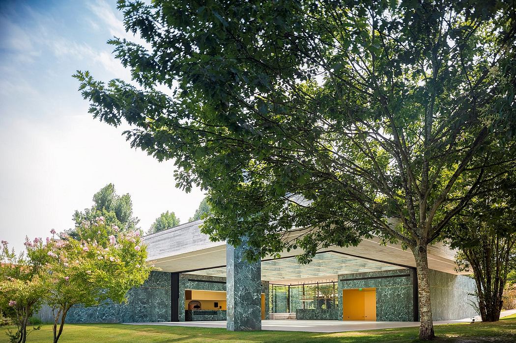 Sleek and modern glass-enclosed structure with a striking green stone facade, nestled among lush trees.