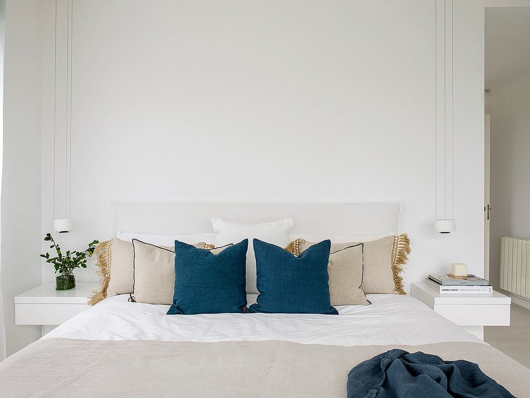 Minimalist bedroom with white walls, modern white bed frame, blue and beige throw pillows.