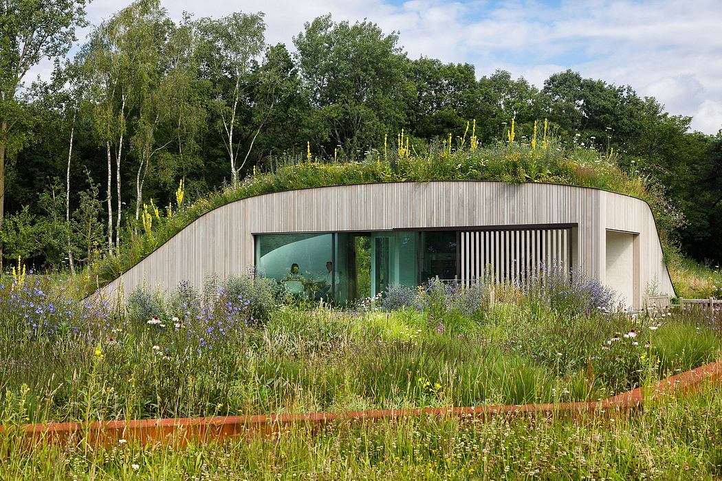Modern, curved metal-clad structure nestled in a lush, natural landscape with large windows.