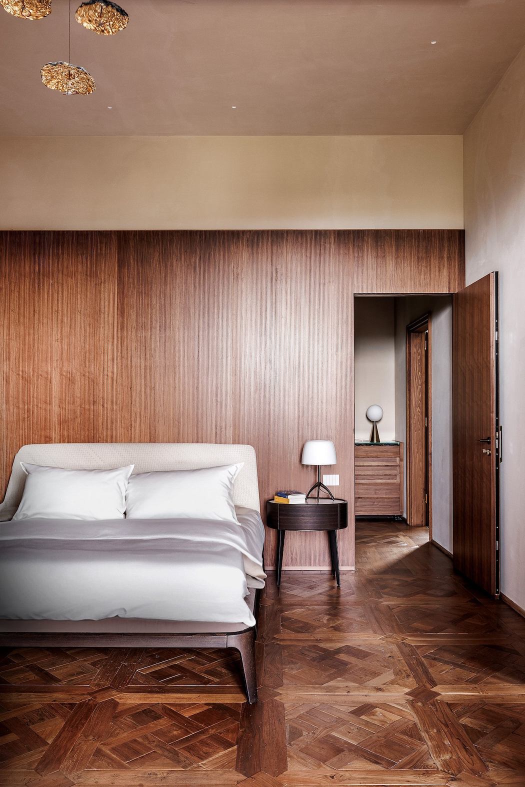 Warm-toned bedroom with wooden paneled walls, herringbone hardwood floor, and modern lighting.
