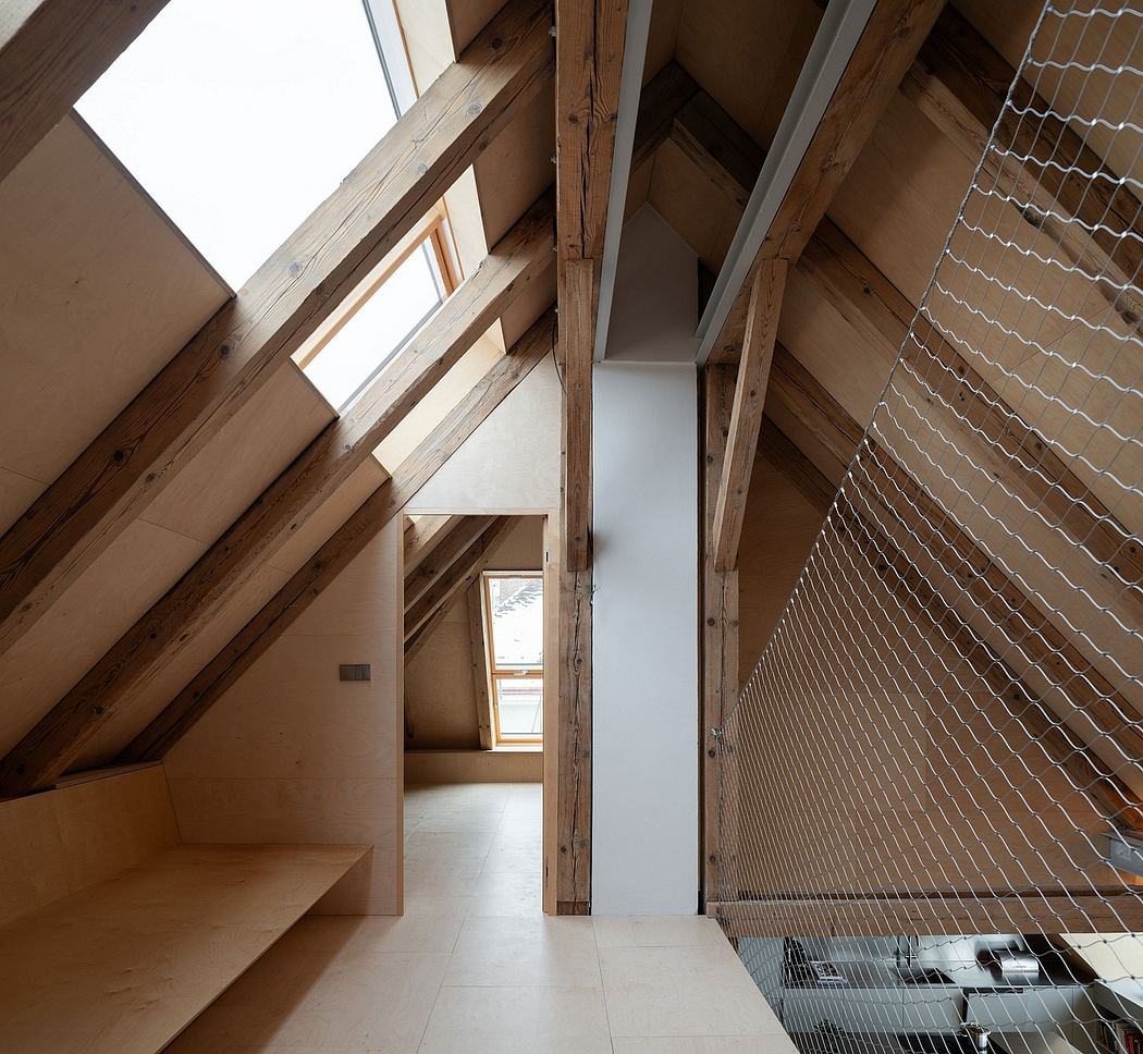 Intricate wooden beam framework in an open, loft-like space with a wire mesh railing.