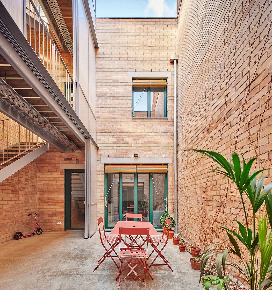 Modernist brick building with metal staircase, patio furniture, and potted plants.