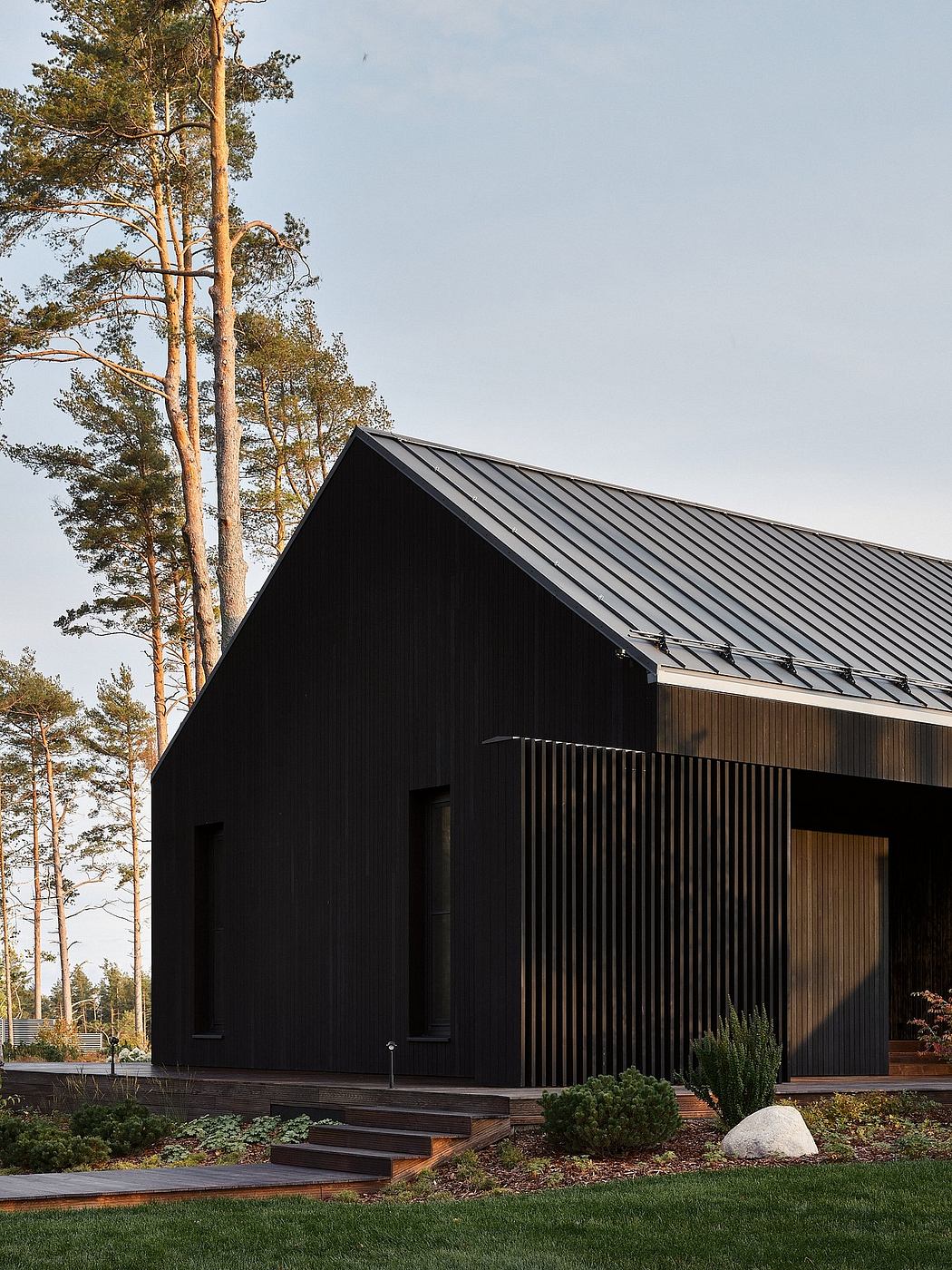 A modern black wooden cabin with a slanted roof and a wooden deck surrounded by trees.
