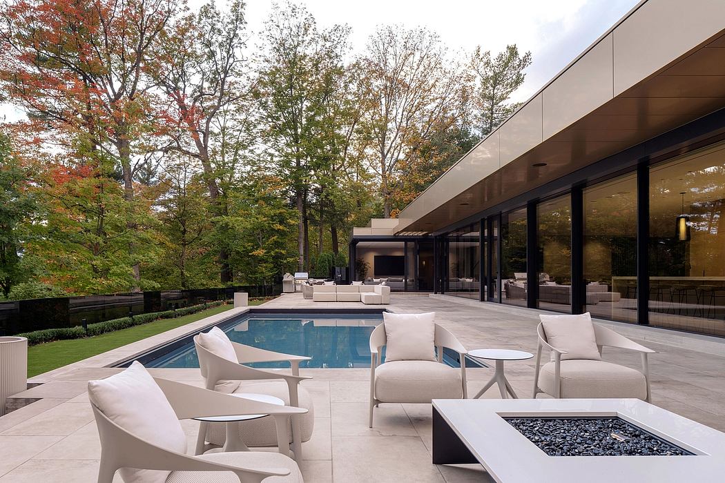 Contemporary glass and stone exterior with outdoor pool, seating, and firepit amidst fall foliage.