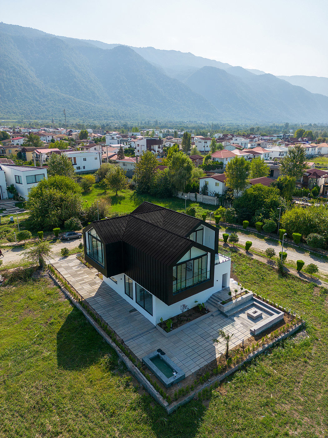 A modern, angular house with large glass panels and a black roof nestled in a lush, verdant setting.