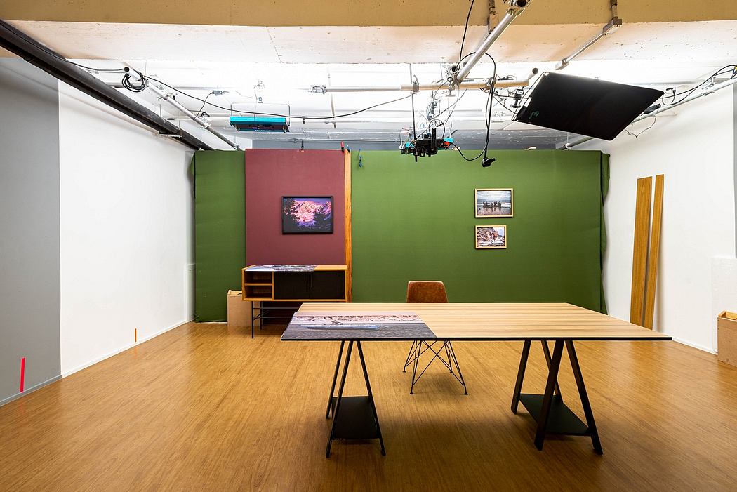 A spacious creative studio with a large wooden table, green and red walls, and various lighting equipment.