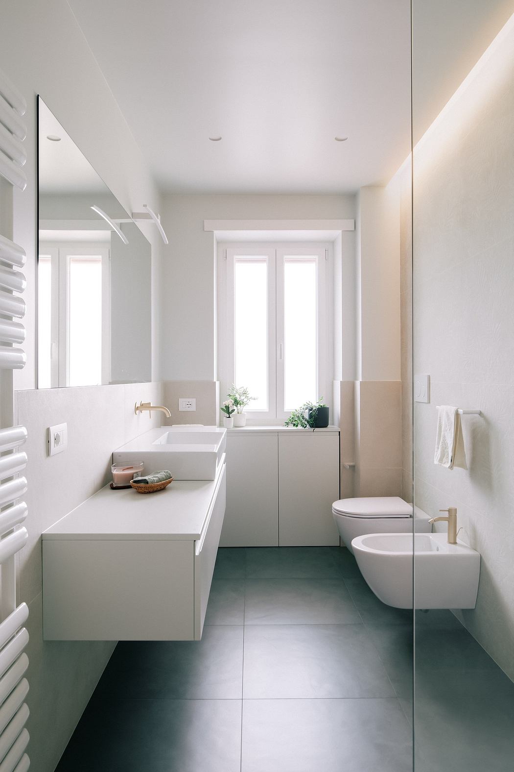 Clean, minimalist bathroom with large white vanity, wall-mounted toilet, and bidet. Bright, airy space with large windows.