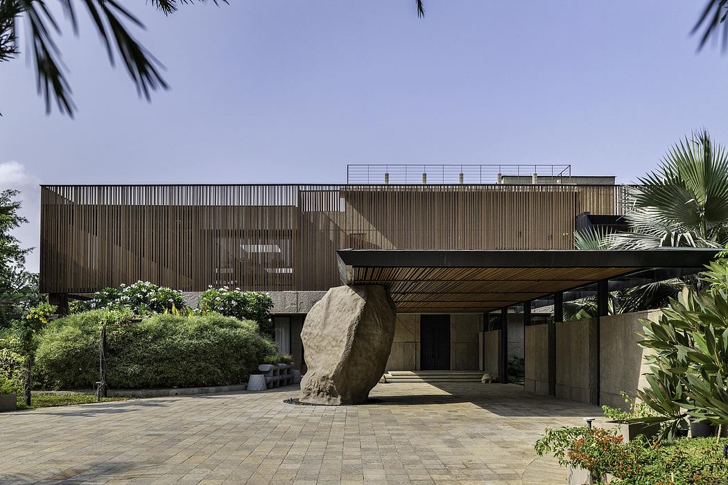 Impressive modern building with wooden slat facade, large boulder, and tropical foliage.