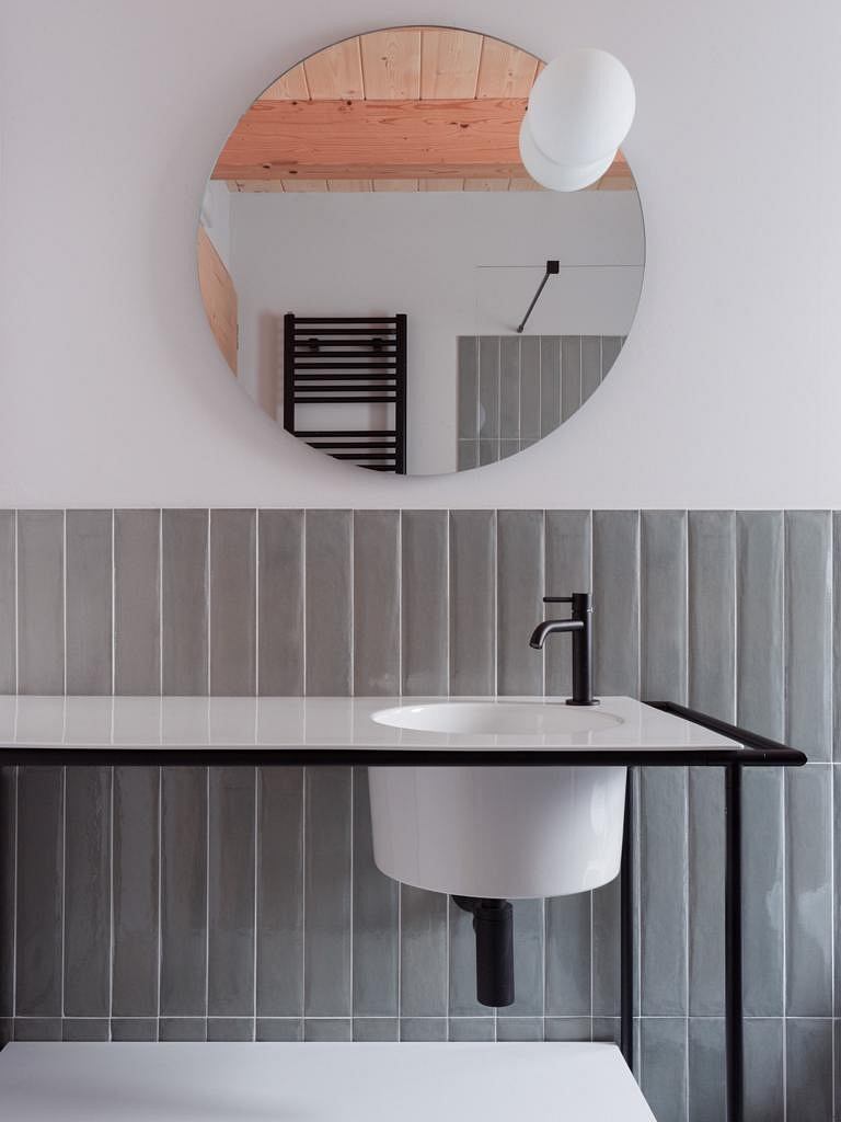 Modern bathroom design featuring circular mirror, black fixtures, and tiled walls.