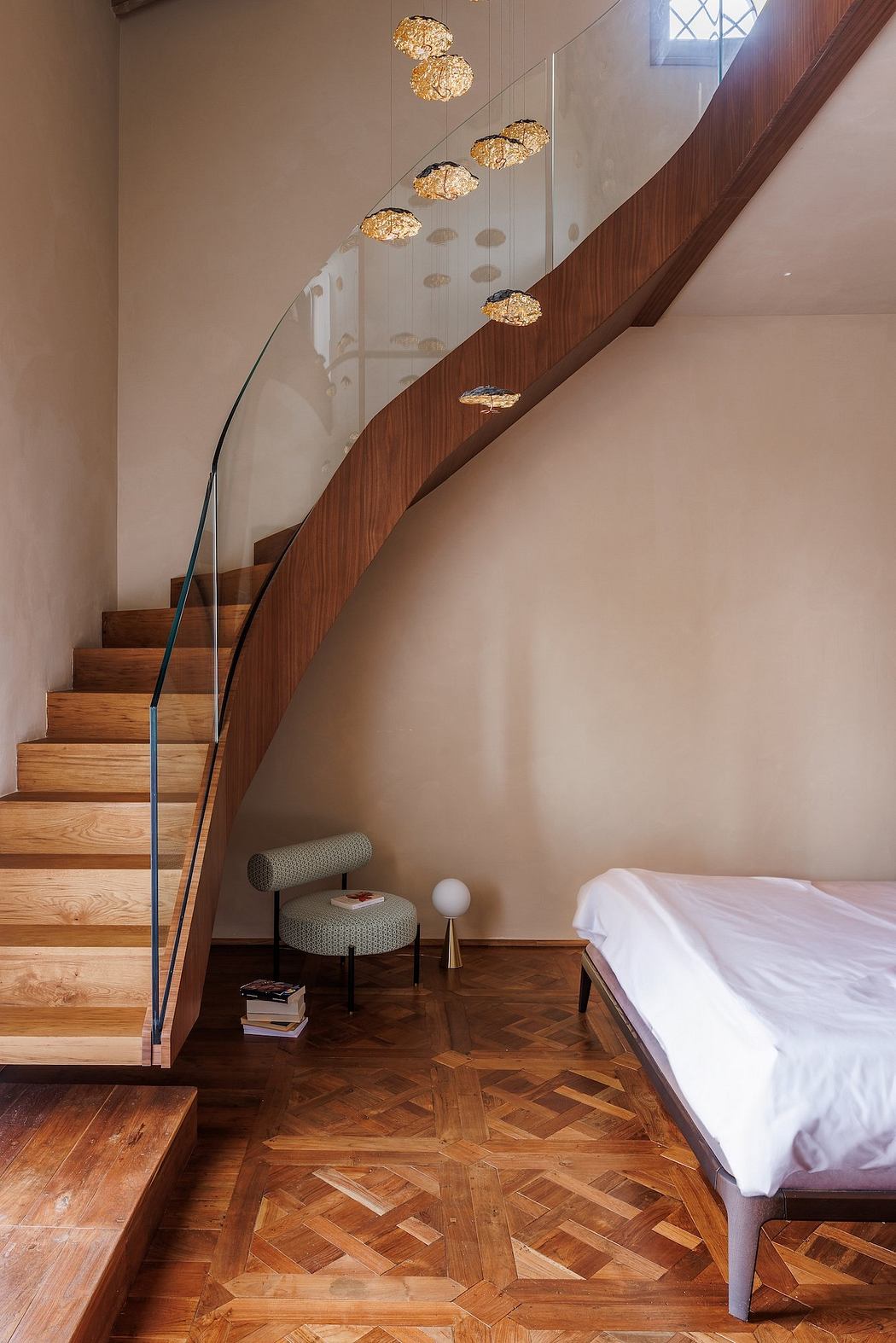Elegant curved wooden staircase with gold-accented pendant lighting, patterned wood flooring.