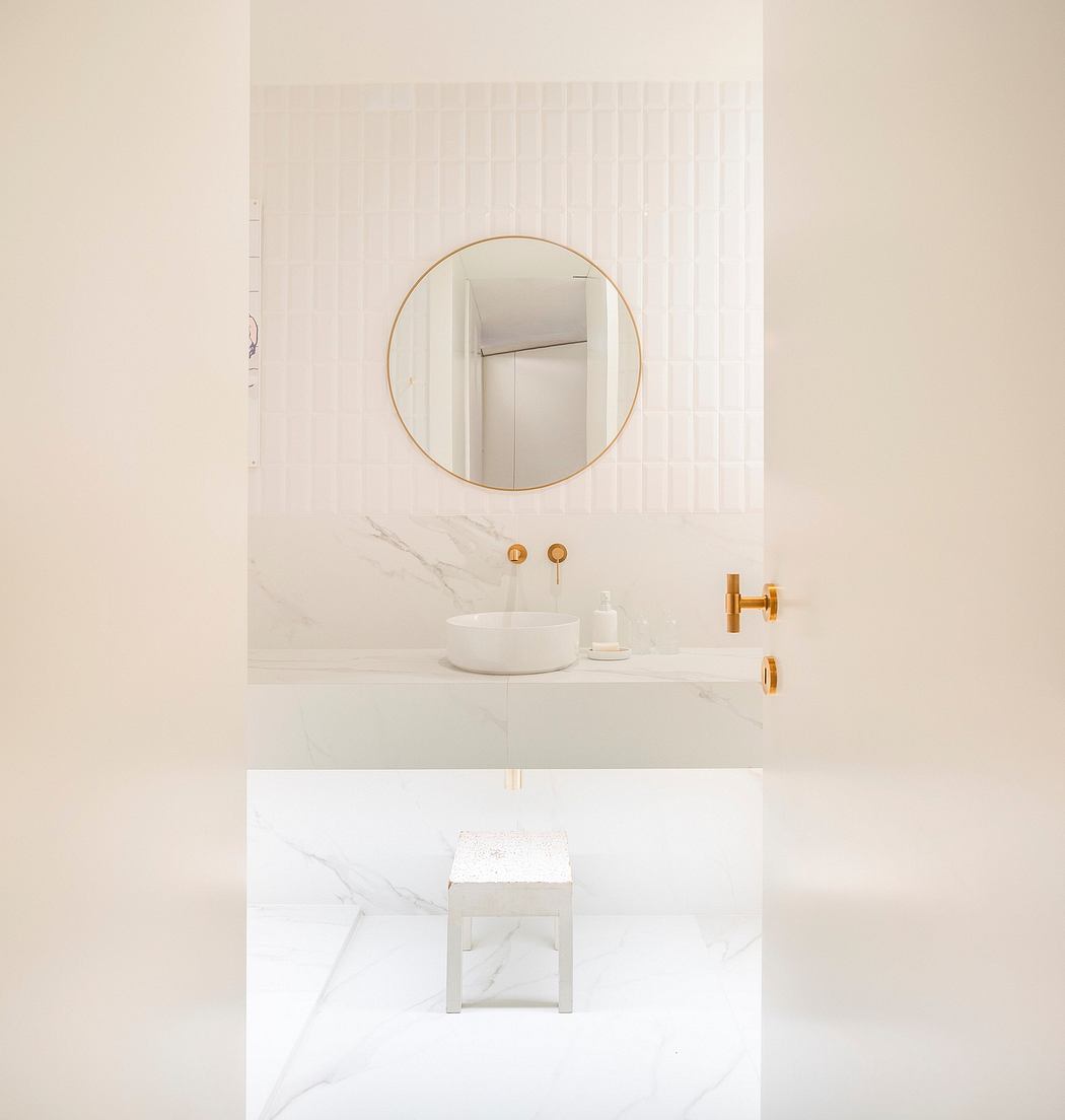 Minimalist bathroom with round gold-framed mirror, marble surfaces, and modern fixtures.