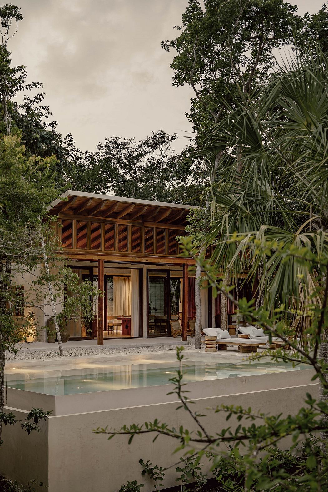 Rustic wooden lodge surrounded by lush tropical foliage, with a tranquil pool reflecting the scene.