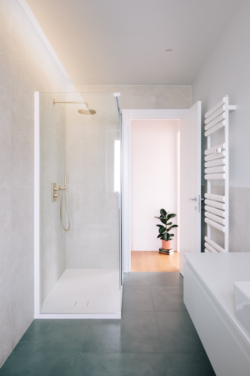 A modern bathroom with a glass shower, gold fixtures, and a potted plant in the corner.