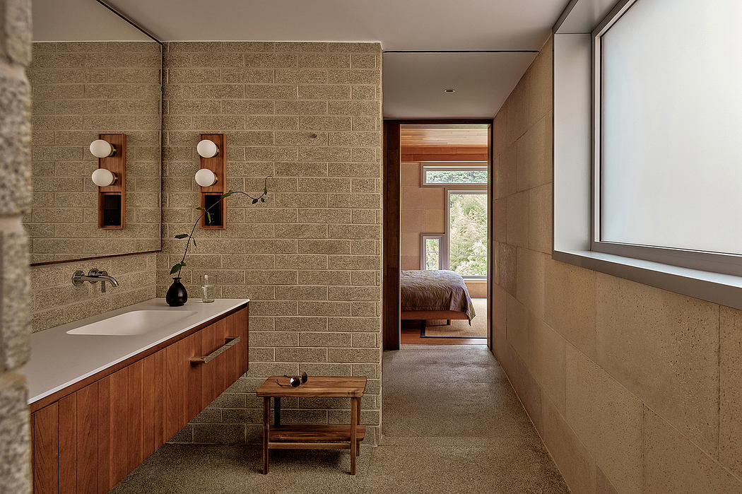 Warm, modern bathroom with wooden vanity, brick walls, and view of bedroom beyond.