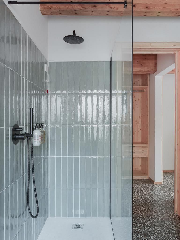 Minimalist bathroom with a rain shower, tiled walls, and exposed wood beams above.