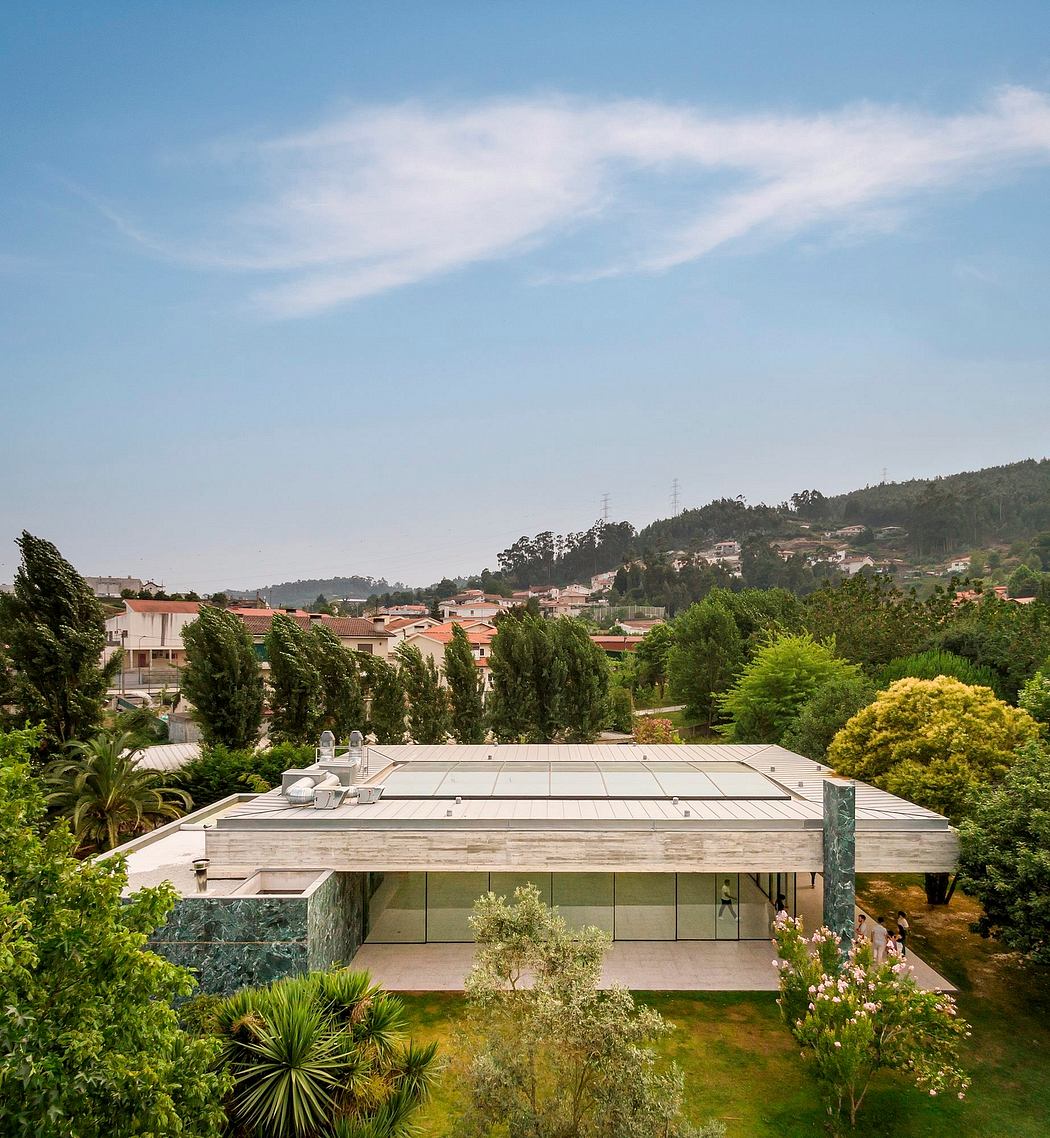 Panoramic view of a modern, glass-fronted building surrounded by lush greenery and residential structures.