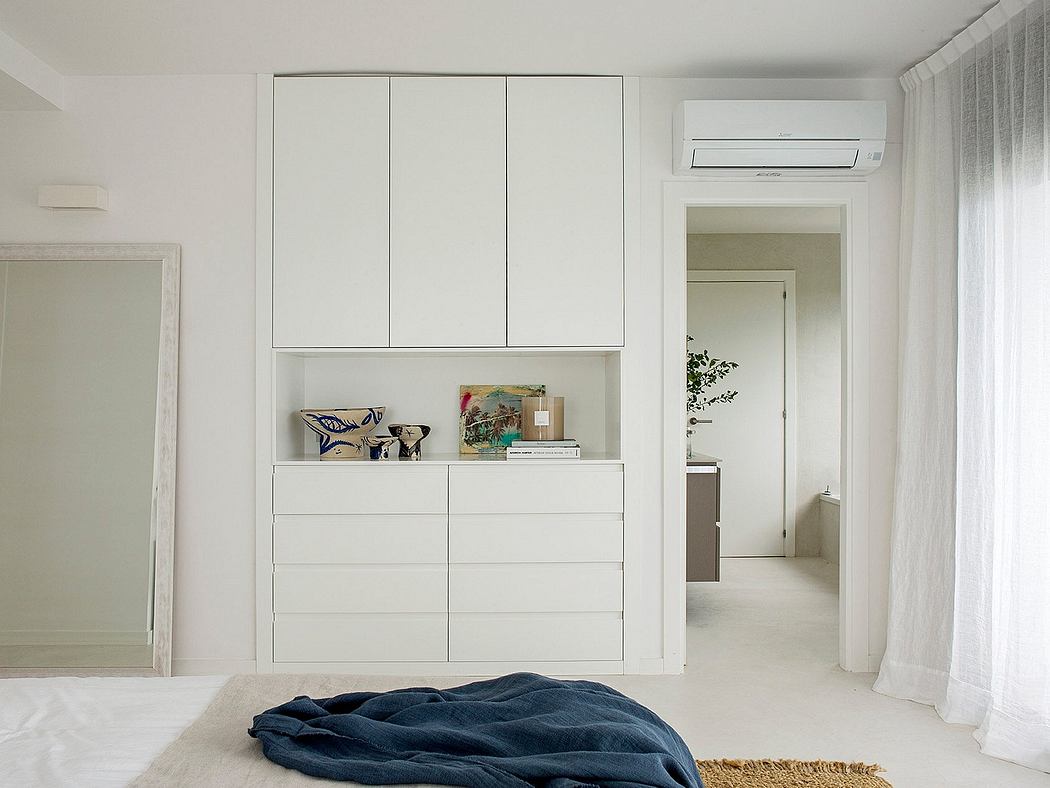 Minimalist bedroom with built-in white cabinets, hardwood flooring, and large window.