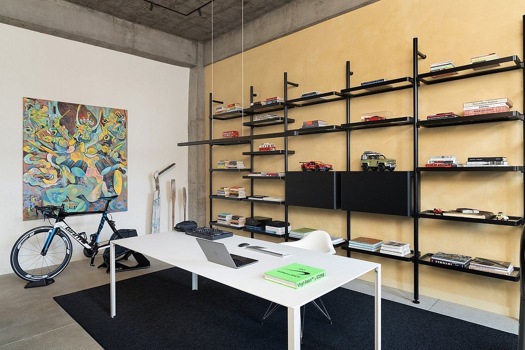 Concrete ceiling, shelving system with books and decor, modern art, and a minimalist workstation.