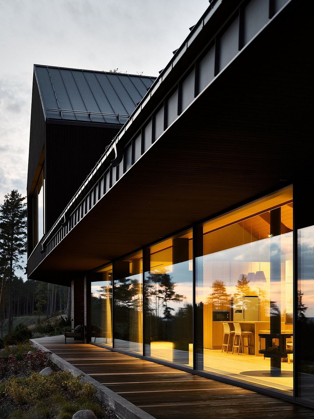 Sleek, modern architecture with expansive glass walls and wooden deck overlooking nature.
