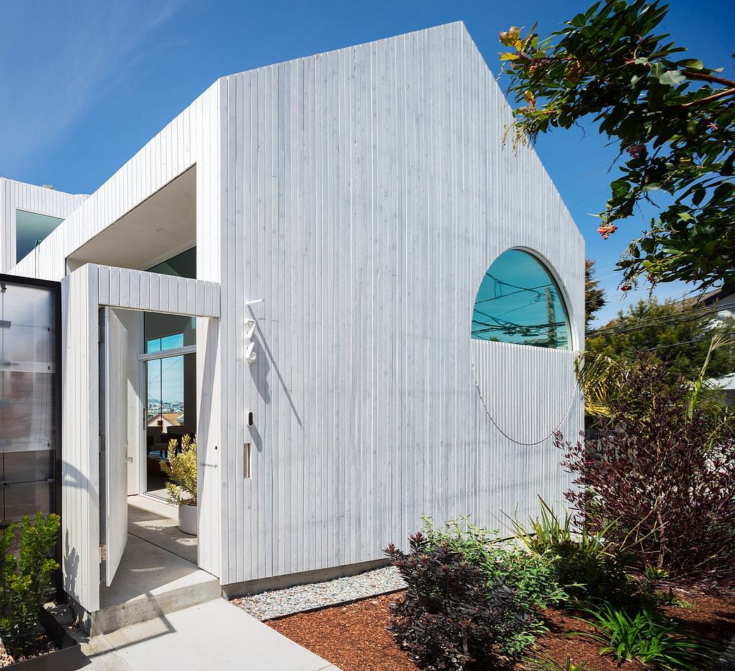 A modern, sleek white building with an arched window and lush landscaping.