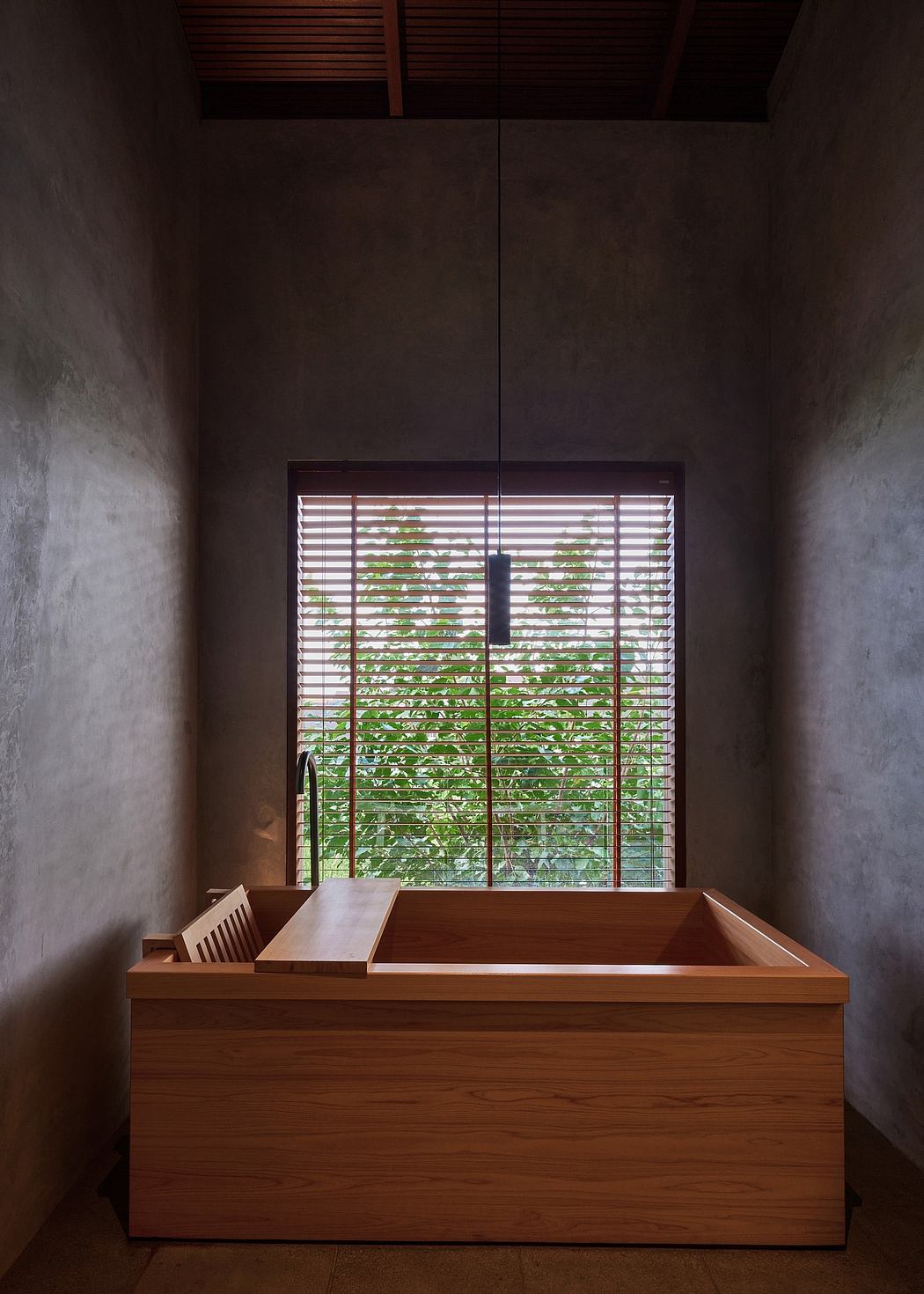 A wooden tub sits below slatted blinds framing a lush outdoor view in this minimalist space.