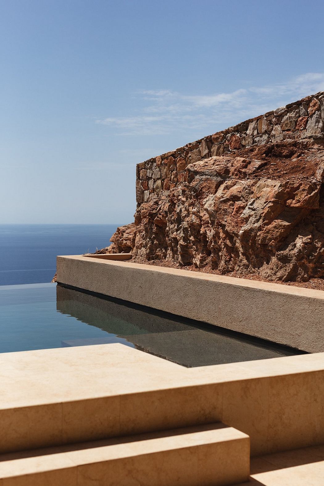 Dramatic rock formation overlooking a tranquil pool against a clear blue sky.