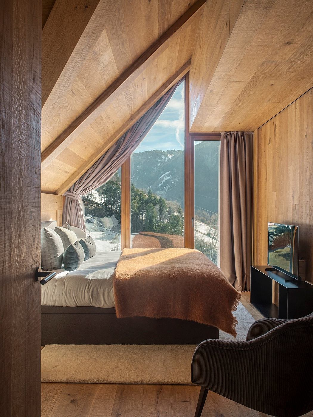 A cozy mountain cabin with a large window offering a scenic view, featuring a plush bed and warm decor.