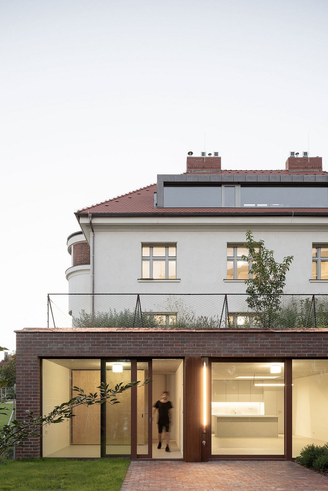 Modern residential building with brick exterior, glass walls, and landscaped front yard.