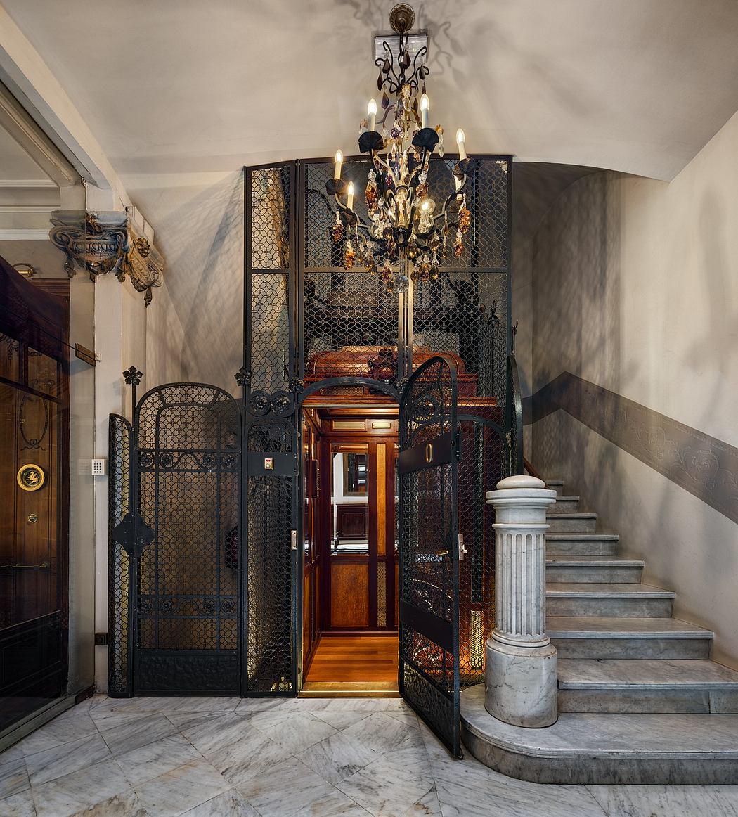 Ornate chandelier, wrought-iron gates, marble stairs, and carved wood details in a grand entryway.