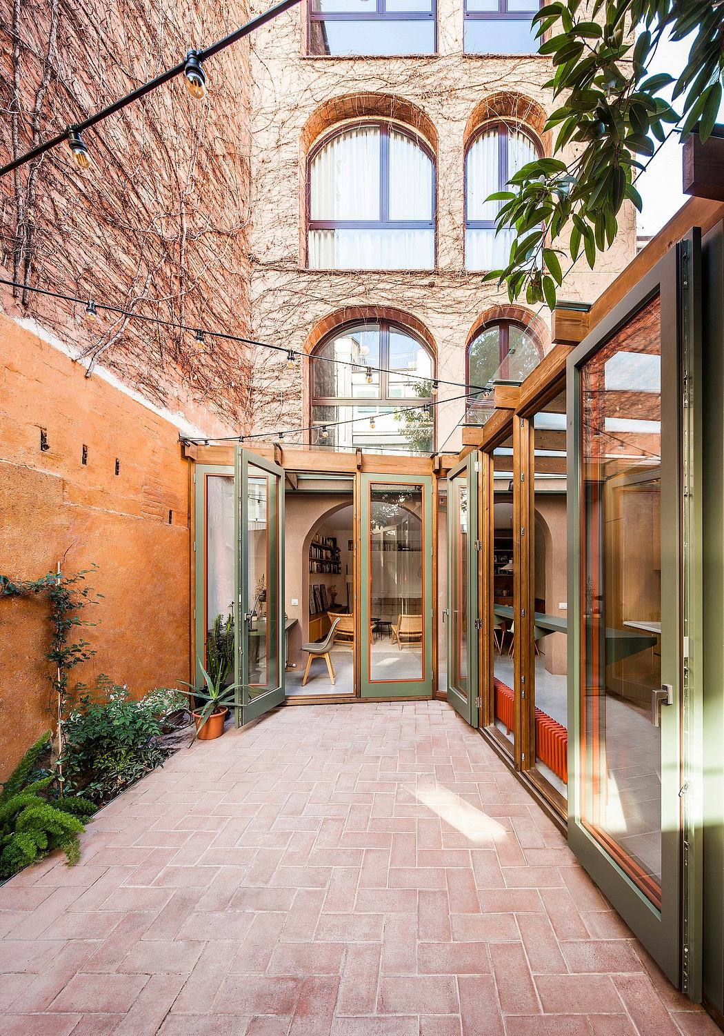 A rustic brick building with arched windows, surrounded by greenery and featuring a warm wood-framed entryway.