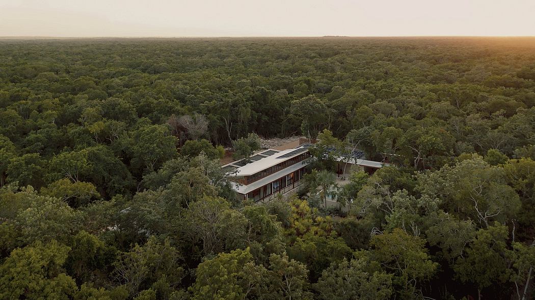 Aerial view of a modern, geometric structure surrounded by a lush, forested landscape.