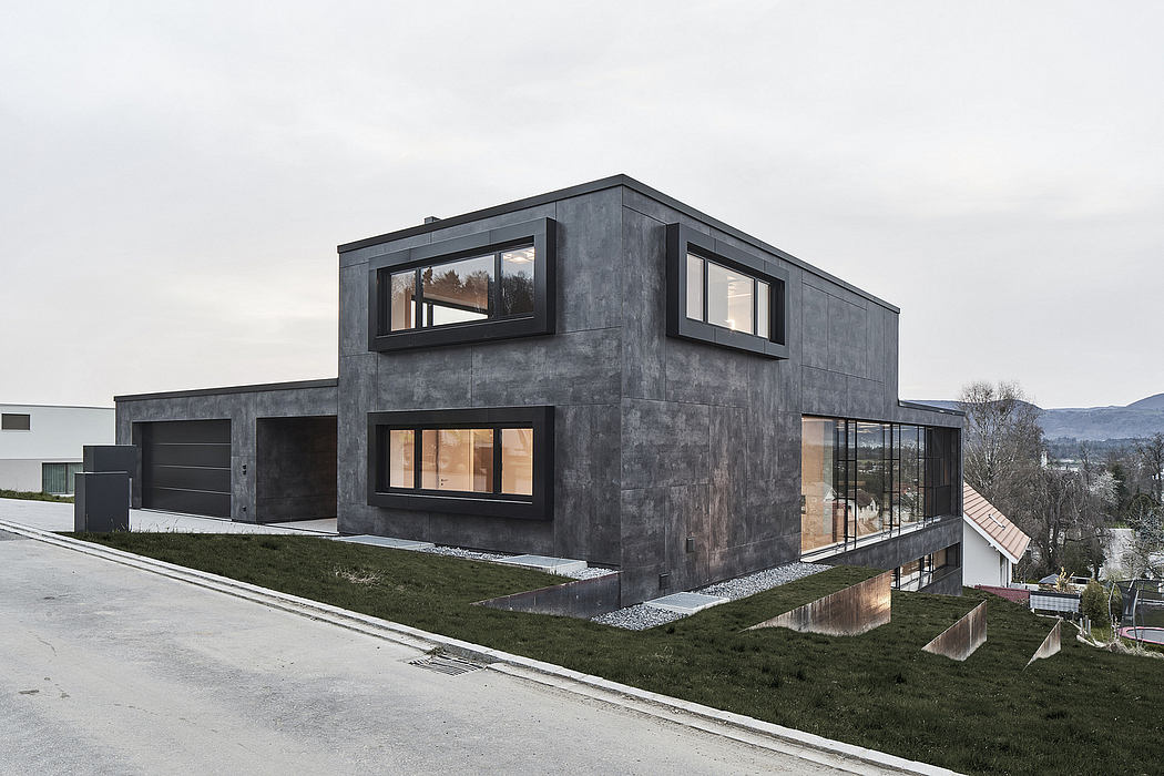 A modern, angular concrete structure with large windows overlooking a grassy landscape.