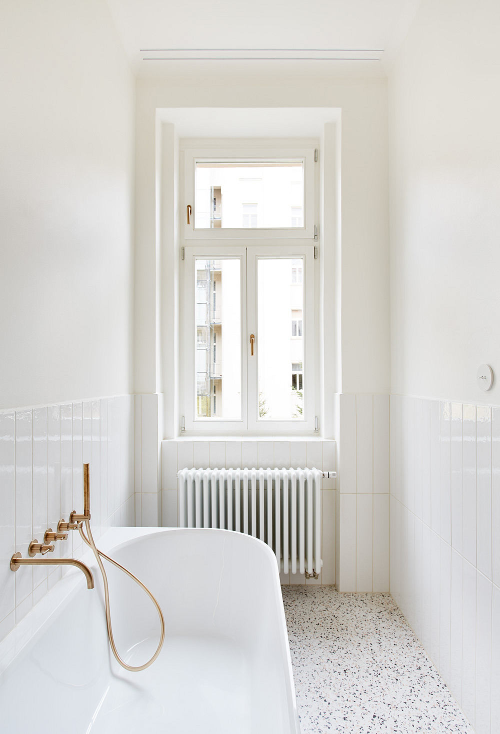 Bright, minimalist bathroom with terrazzo floor, freestanding tub, and large window.