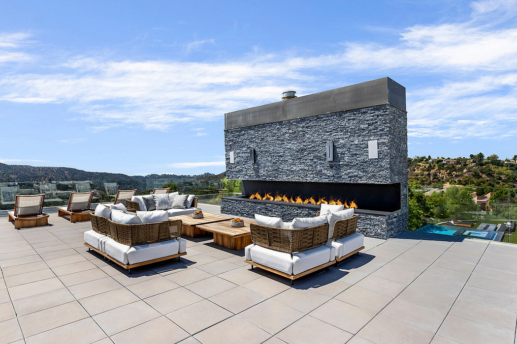 Outdoor terrace with cozy seating arrangements and a large stone fireplace against a scenic backdrop.