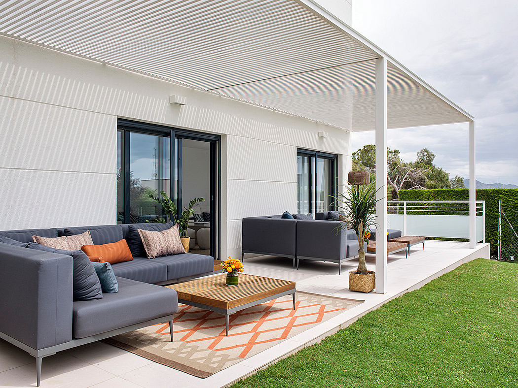 Contemporary outdoor living space with gray sofas, wooden coffee table, and lush green lawn.