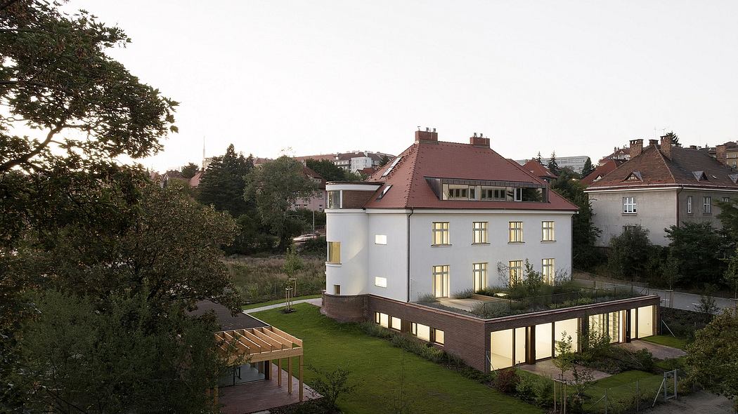 A multi-story residential building with a red-tiled roof, surrounded by a grassy lawn and lush foliage.