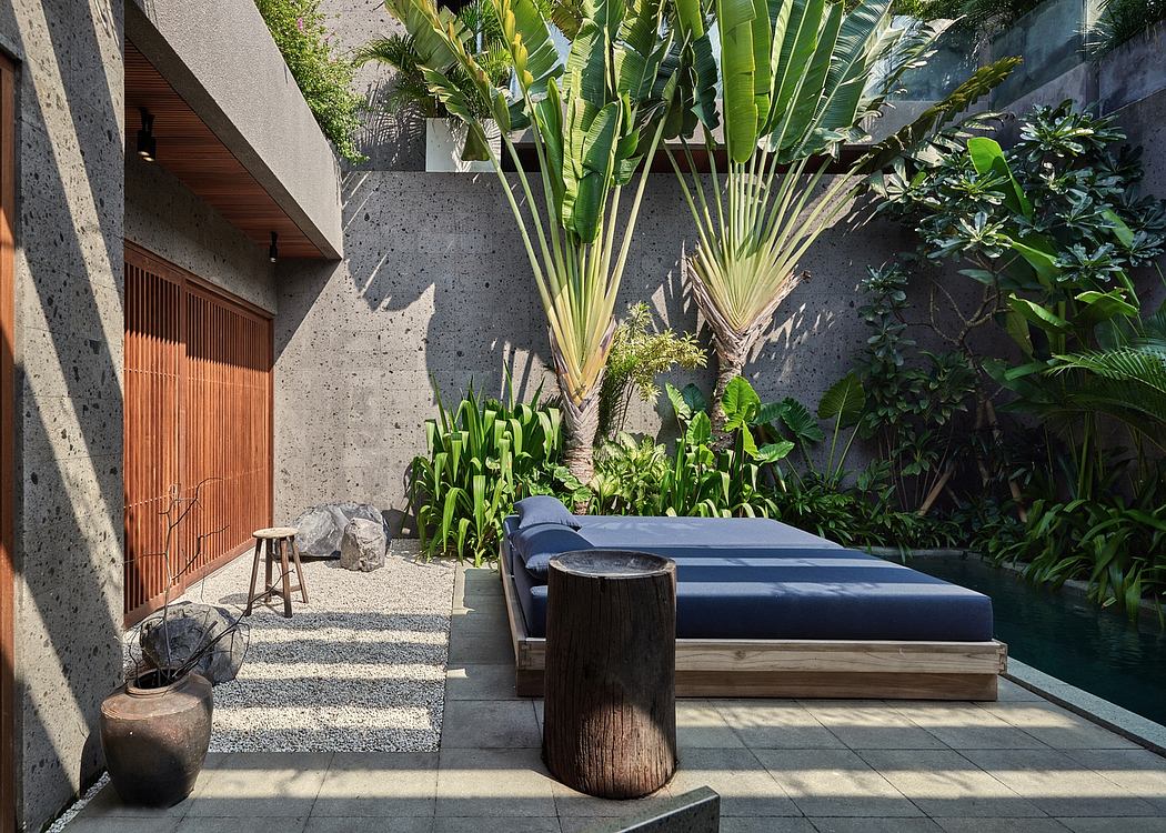 Lush tropical garden surrounds a modern patio with a wooden daybed and simple furnishings.